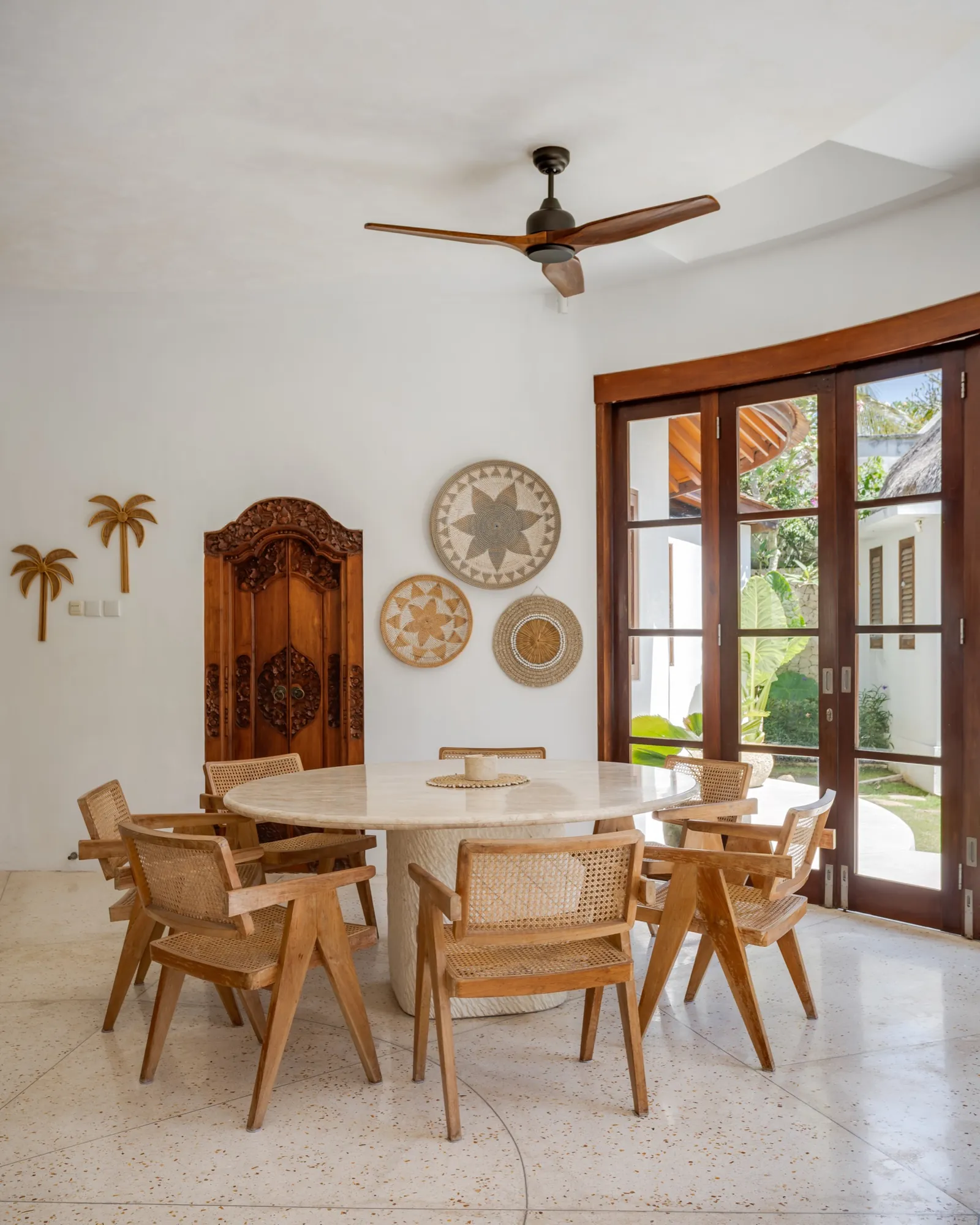 Interior dining area at Madu Bungalow Bingin, carved timber door and rattan chairs around a stone table